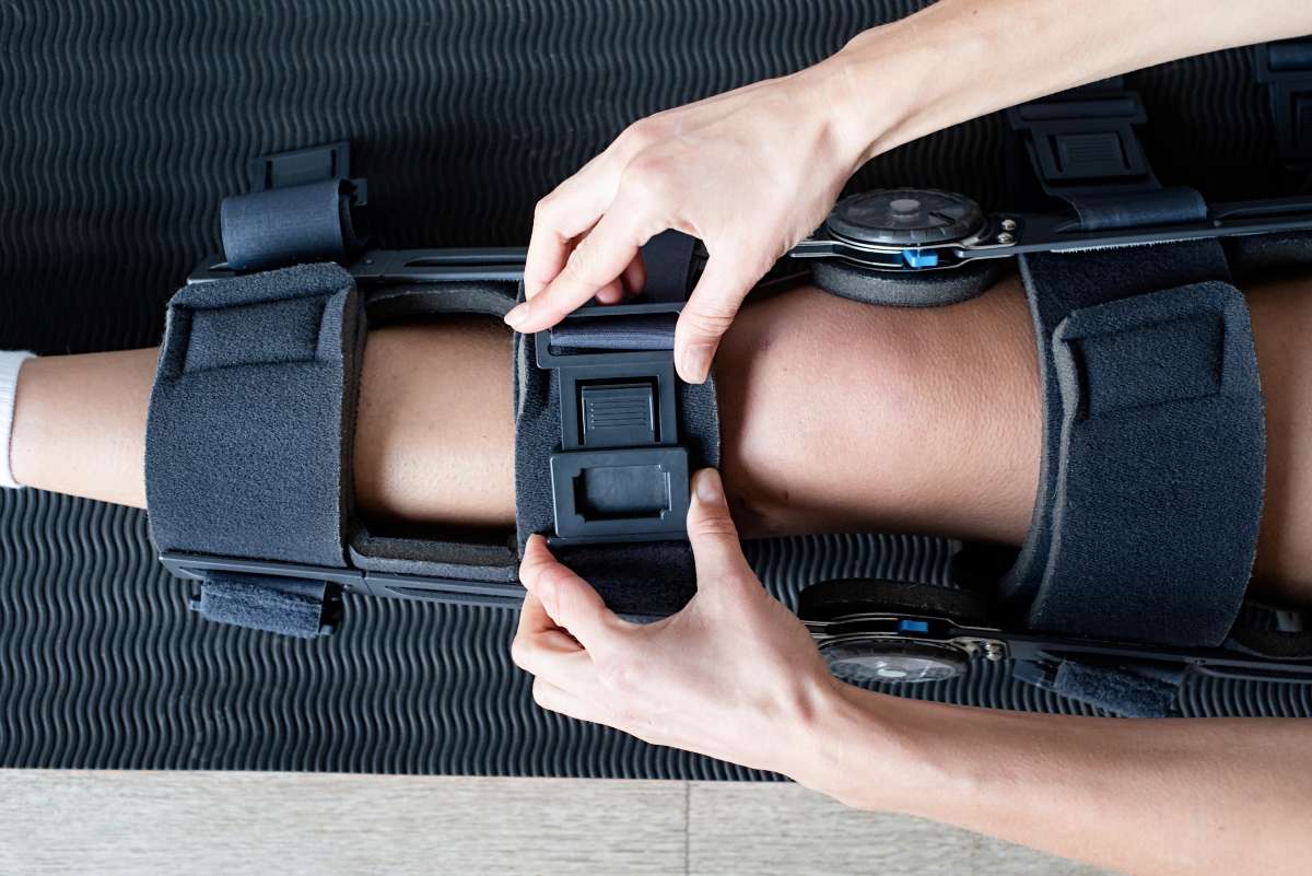 Clinician fastening a hinged custom knee brace onto a patient's leg
